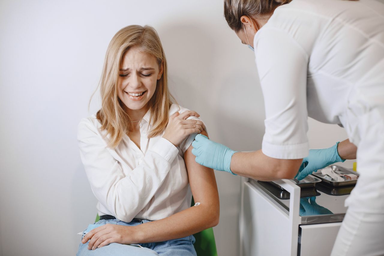 Blonde woman receives vaccination from healthcare professional indoor.